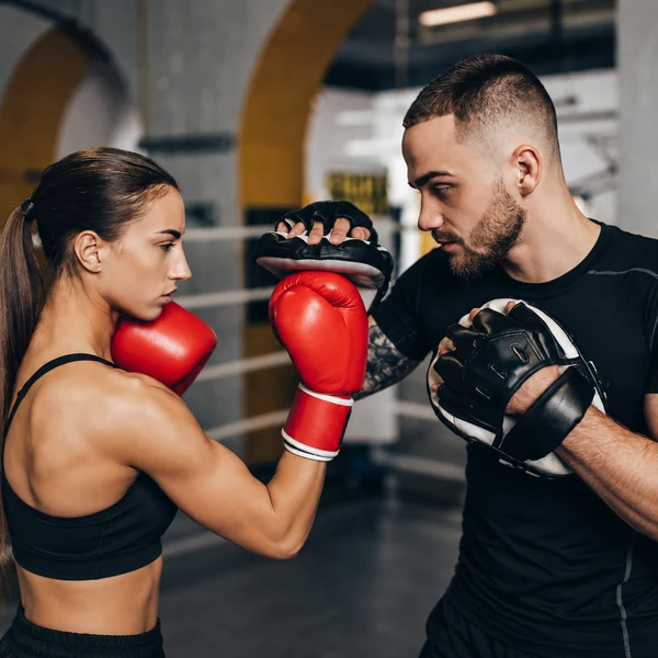 Female boxer practising pad work with a coach holding focus mitts